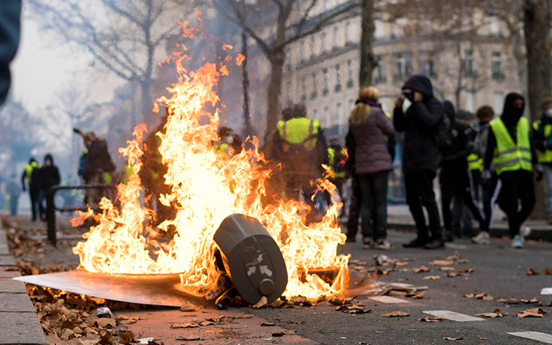 photo of fire in front of people wearing yellow vests as part of the gilets jaunes movement